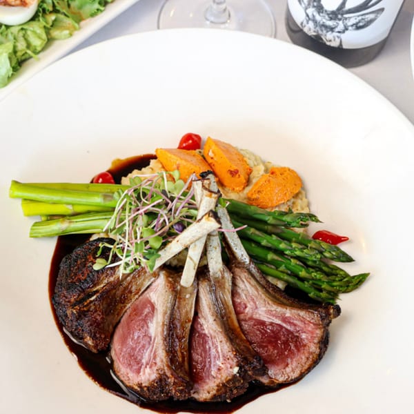 Plated lamb chops with asparagus, sweet potato, microgreens, and a dark sauce.