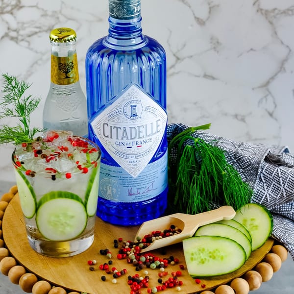 A Waypoint Seafood & Grill gin cocktail with cucumber, dill, and peppercorns, alongside gin and tonic bottles.