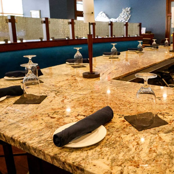 Waypoint Seafood & Grill bar with granite countertop, set with plates, rolled napkins, and inverted wine glasses.