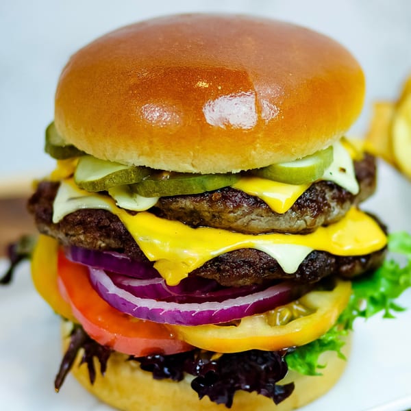 A towering double cheeseburger with pickles, onions, tomatoes, and lettuce on a brioche bun.