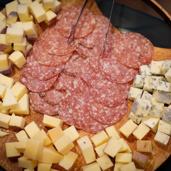 A wooden board with sliced salami, cubed yellow cheese, and cubed blue cheese.