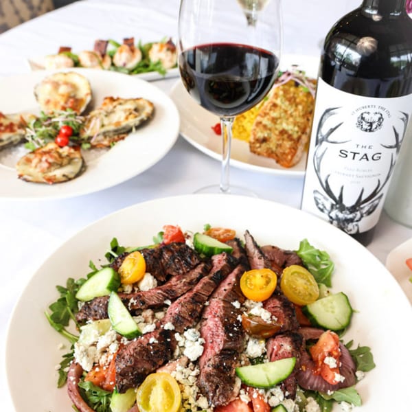 Steak salad with tomatoes, cucumbers, and feta, alongside oysters, shrimp skewers, and red wine.