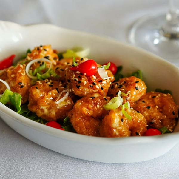 Crispy honey-glazed shrimp with sesame seeds, red chilies, and green onions in a white bowl.