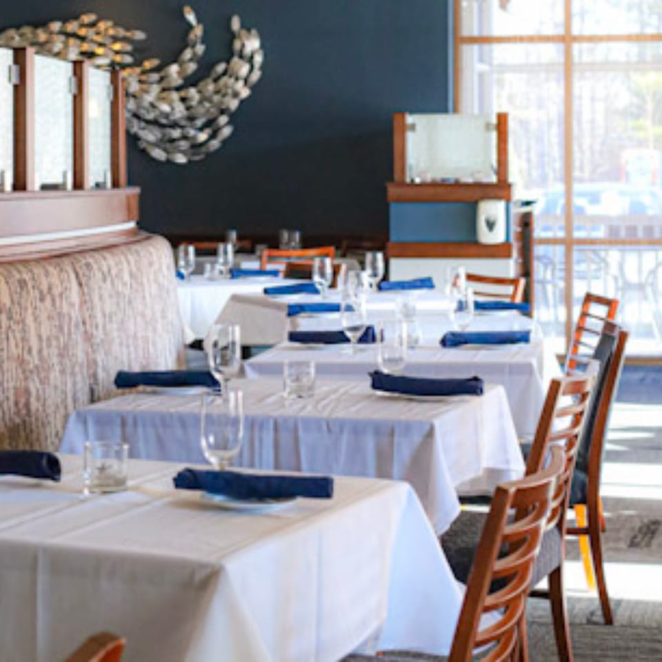 Waypoint Seafood & Grill dining room with set tables, blue napkins, and a fish art installation.