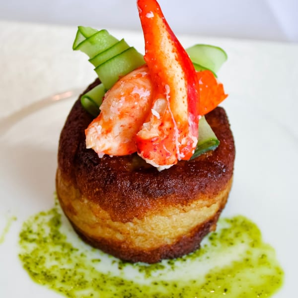 Golden-brown pastry topped with vibrant red lobster meat and thinly sliced green cucumbers, drizzled with green sauce.