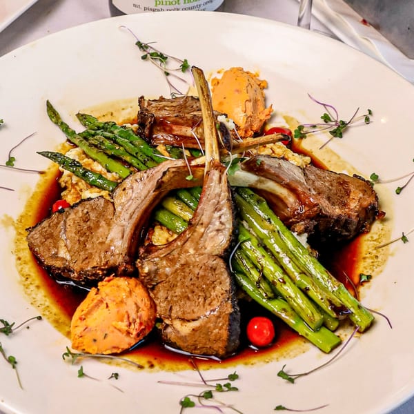 Four lamb chops with asparagus, risotto, and sweet potato puree on a white plate.