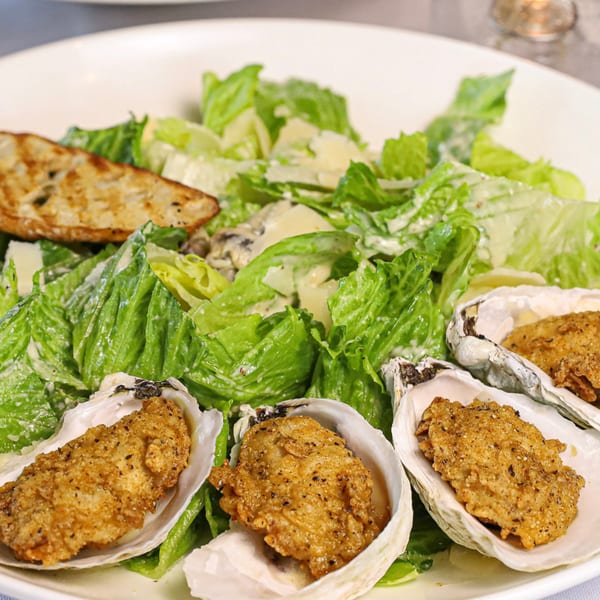 Caesar salad with croutons and four fried oysters in their shells on a white plate.